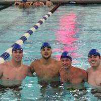 Four swimmers in the pool, smiling for a photo